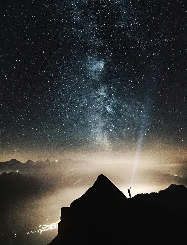 Silhouette of person looking at night sky while standing on mountain